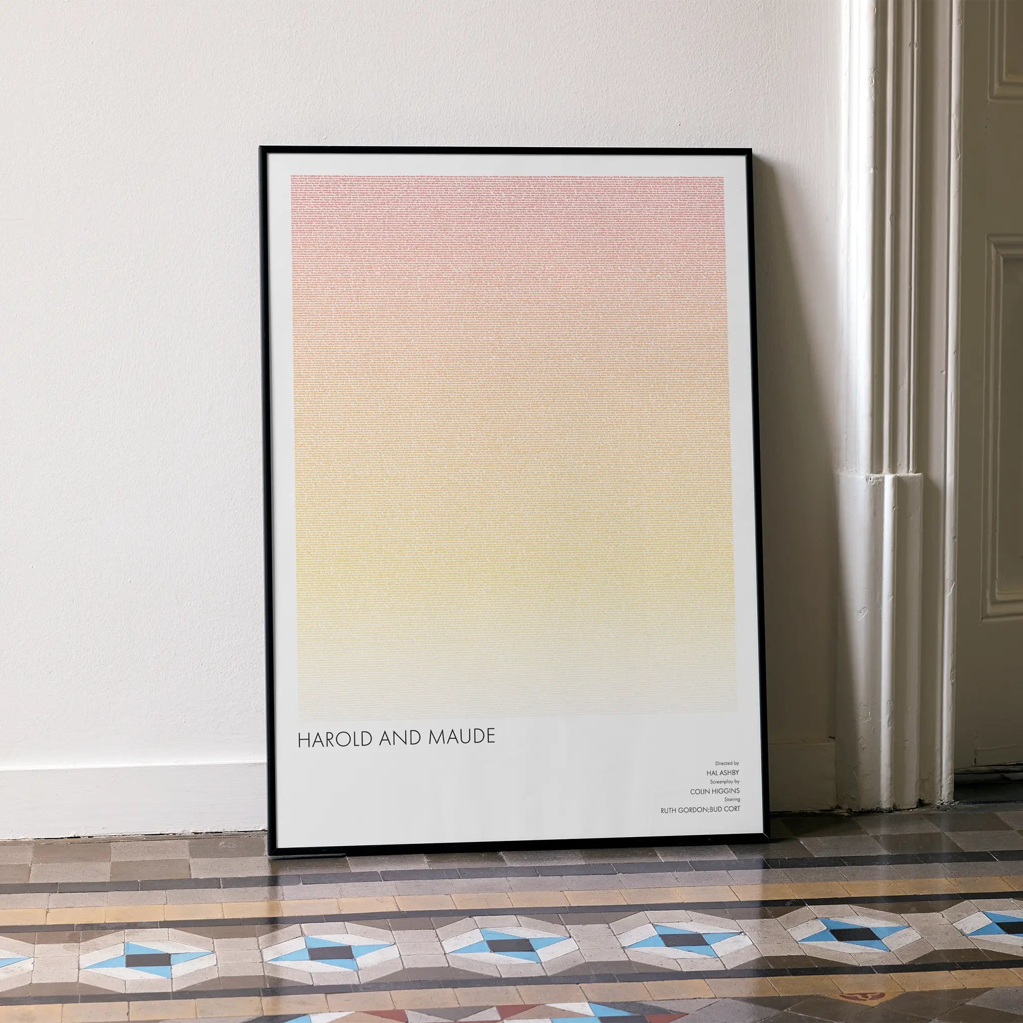 A framed Harold and Maude movie script poster leaning against a wall in a minimalist interior.