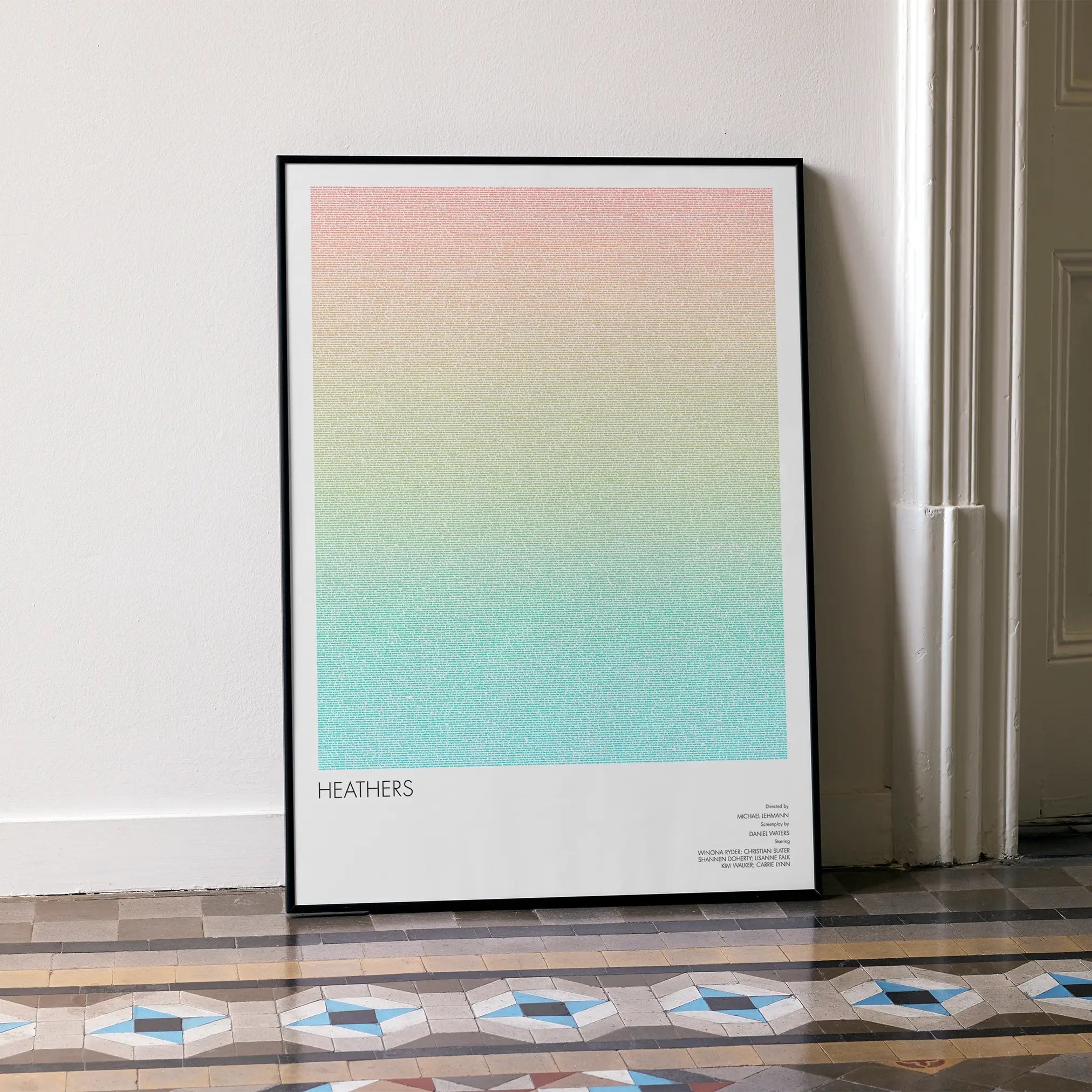 A framed Heathers movie script poster leaning against a wall in a minimalist interior.