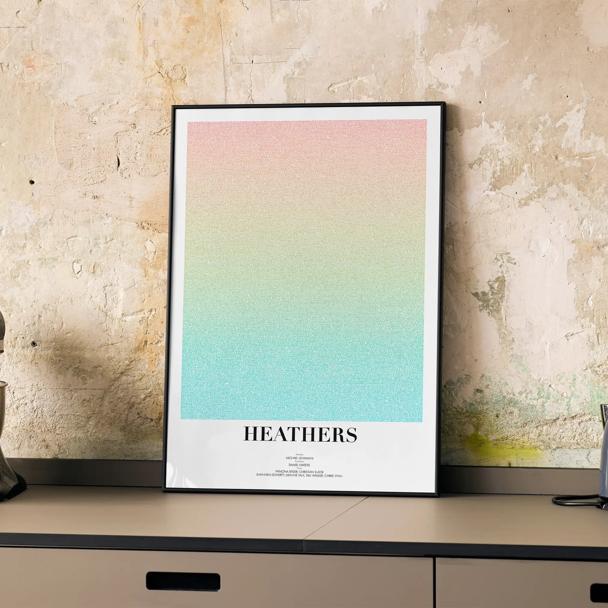A framed Heathers movie script poster displayed on a cabinet in a minimalist interior.