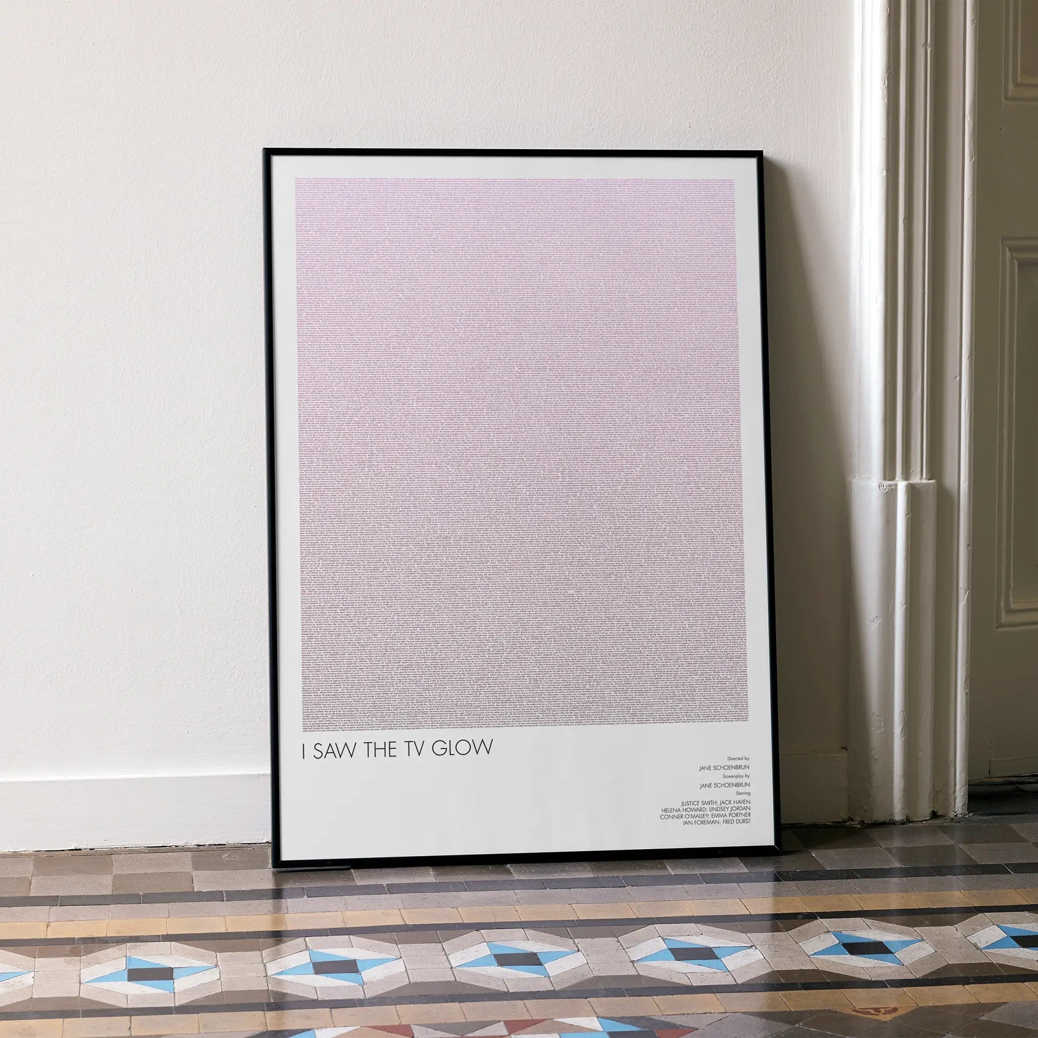 A framed I Saw the TV Glow movie script poster leaning against a wall in a minimalist interior.