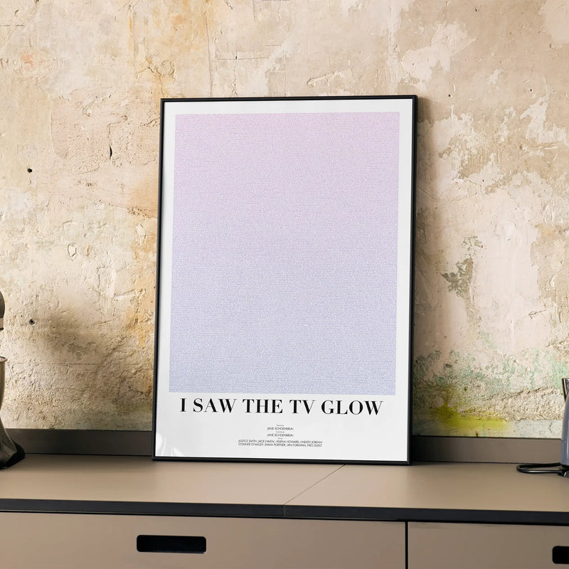A framed I Saw the TV Glow movie script poster displayed on a cabinet in a minimalist interior.