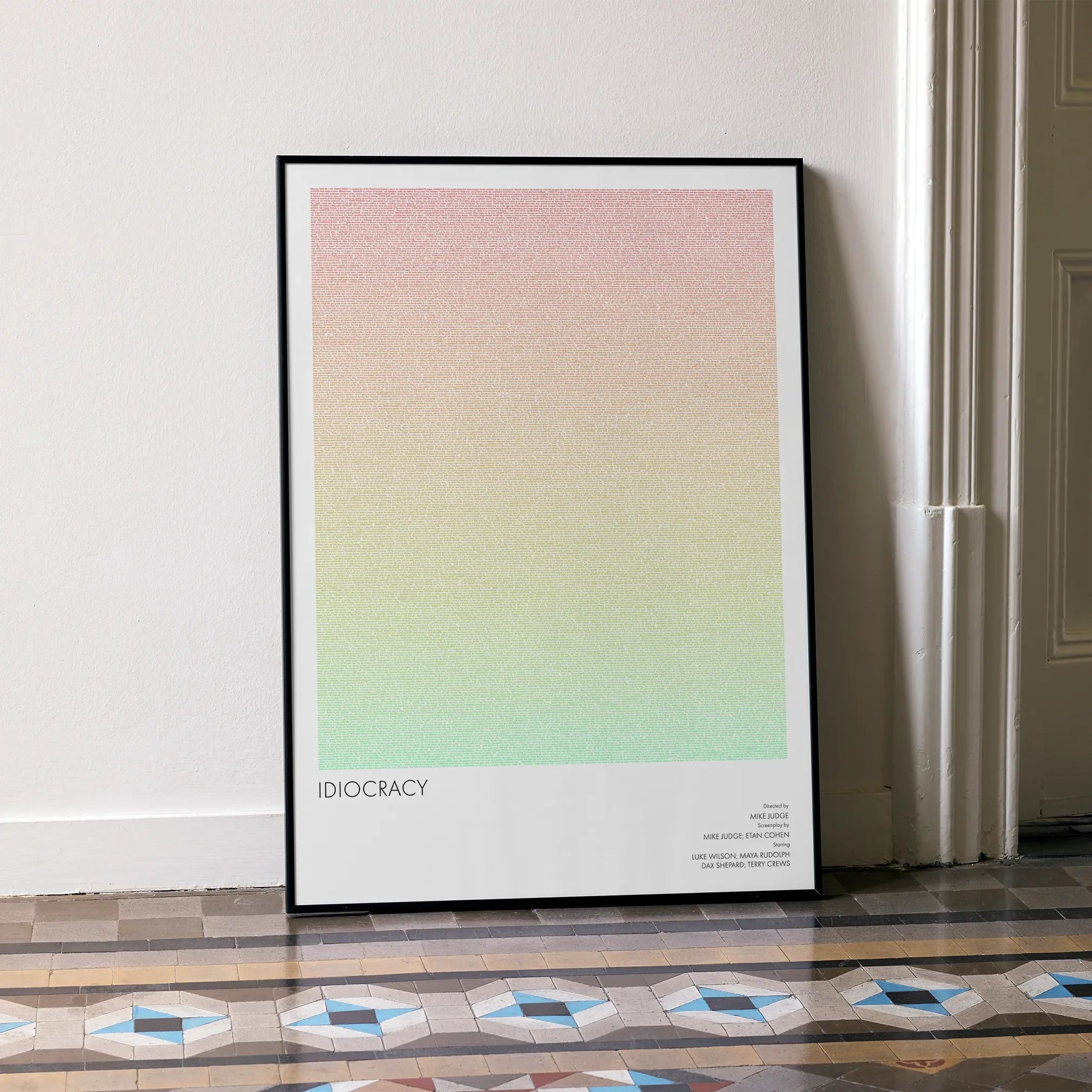 A framed Idiocracy movie script poster leaning against a wall in a minimalist interior.