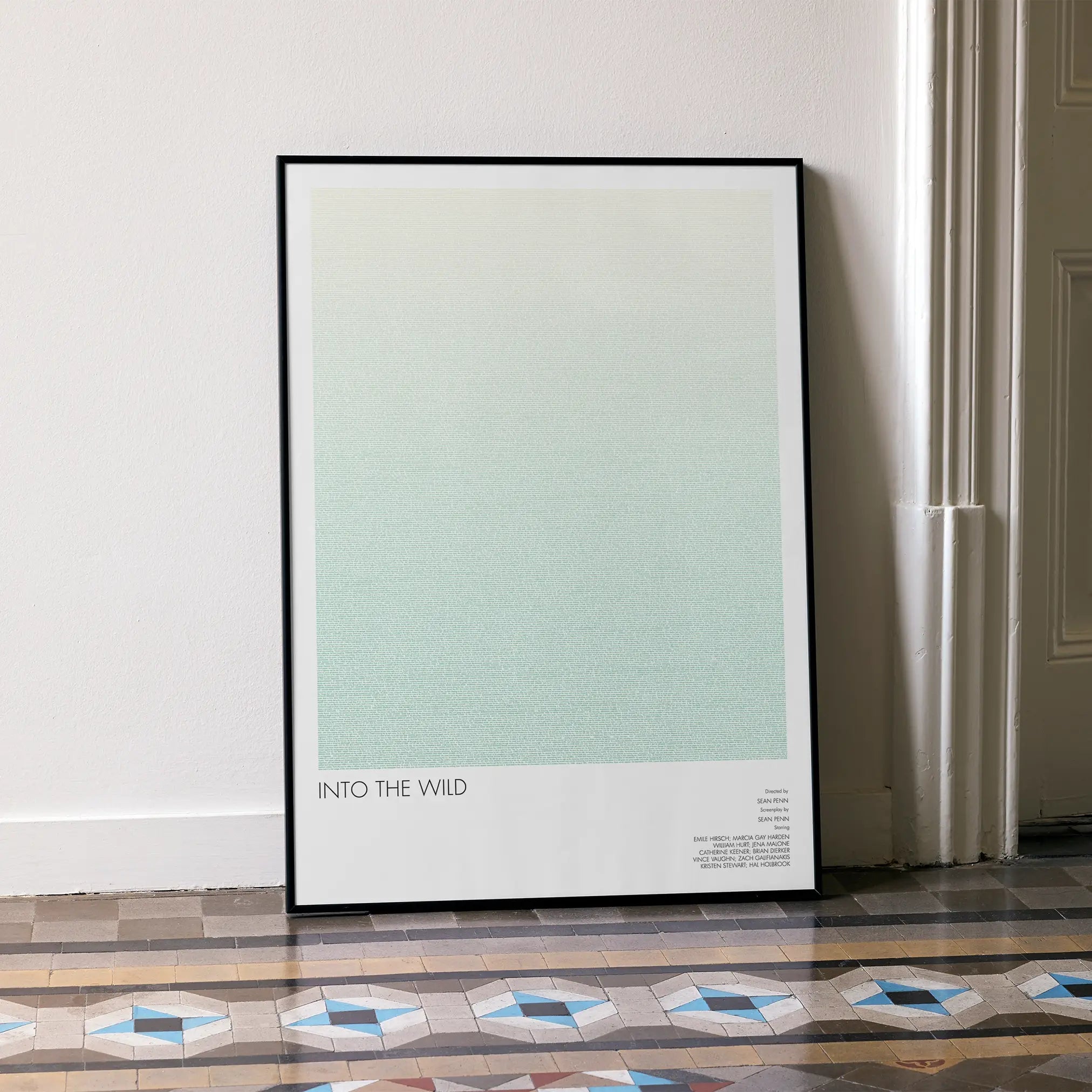 A framed Into the Wild movie script poster leaning against a wall in a minimalist interior.