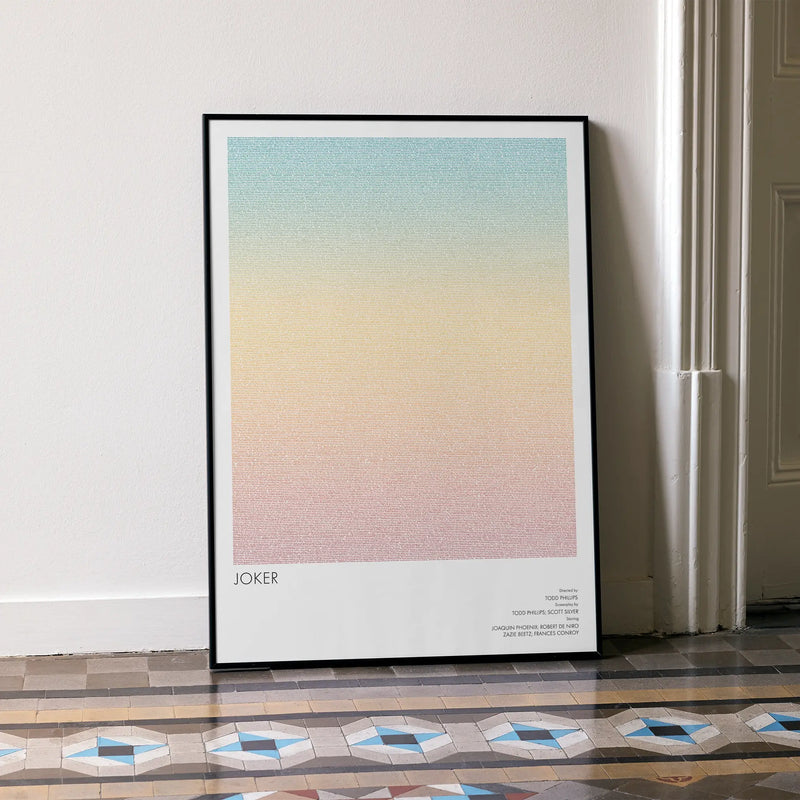 A framed Joker movie script poster leaning against a wall in a minimalist interior.
