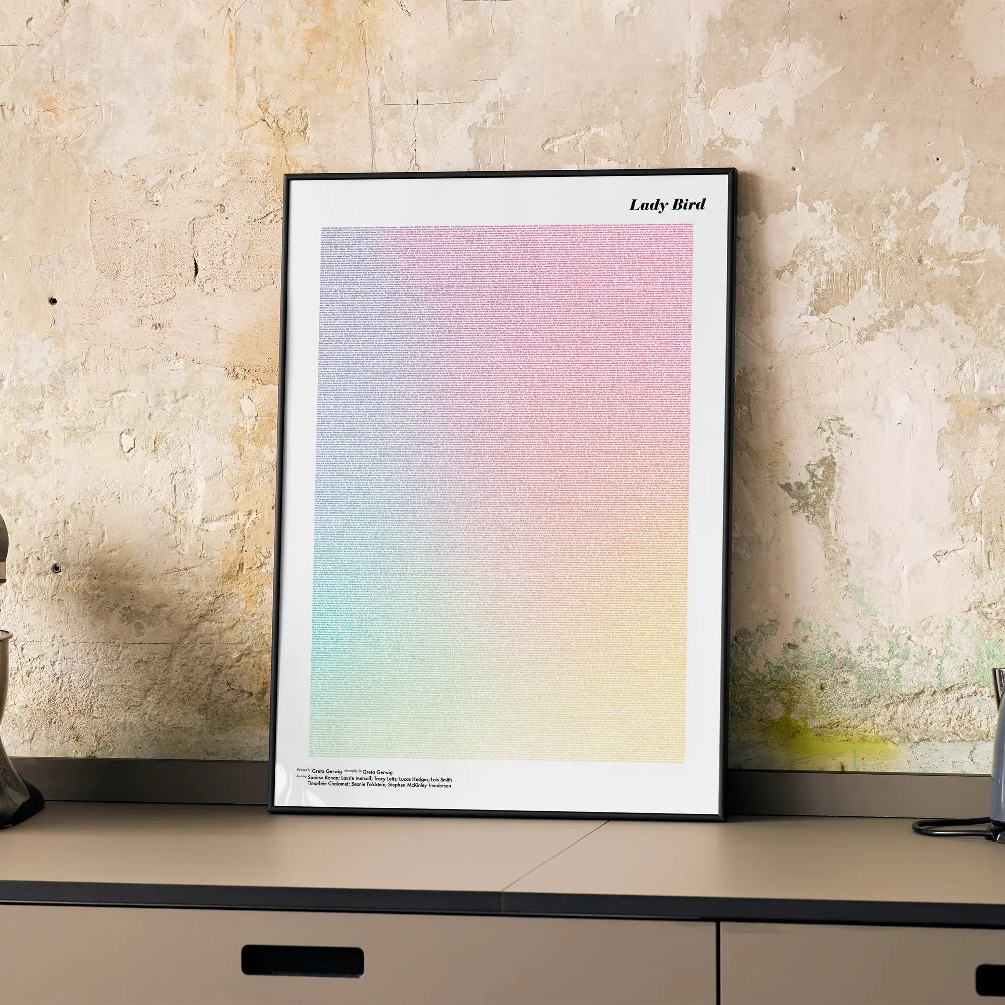 A framed Lady Bird movie script poster displayed on a cabinet in a minimalist interior.