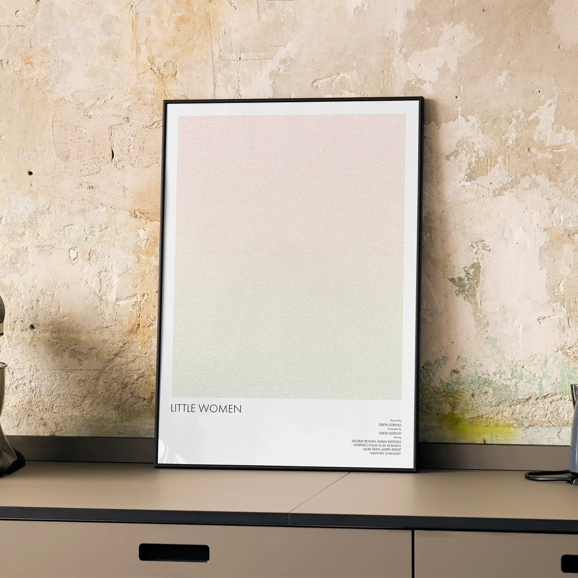 A framed Little Women movie script poster displayed on a cabinet in a minimalist interior.
