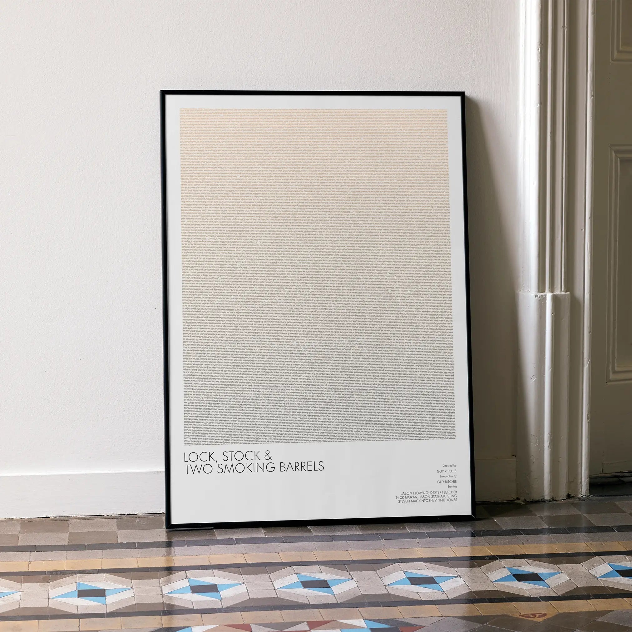 A framed Lock, Stock and Two Smoking Barrels movie script poster leaning against a wall in a minimalist interior.