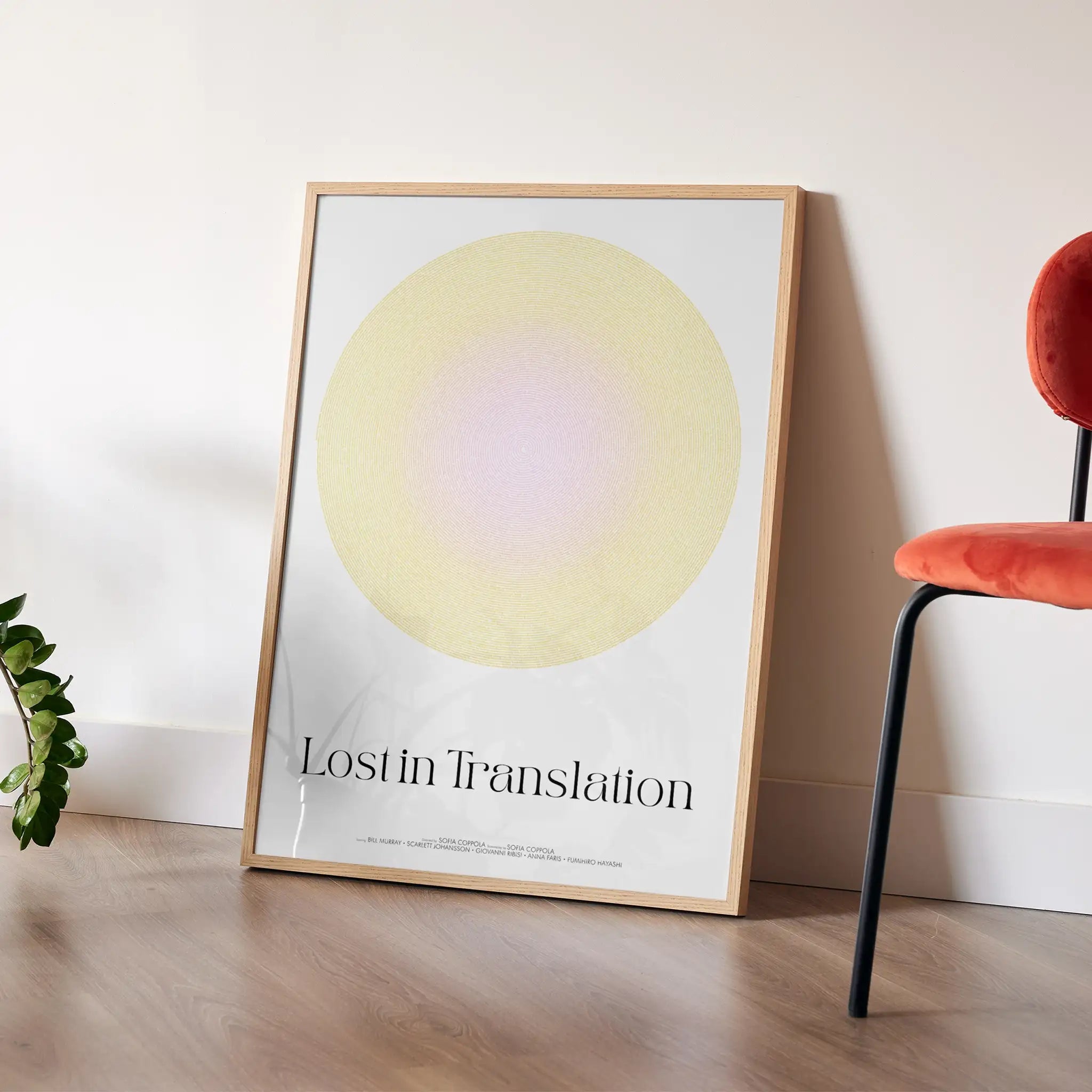 Framed artwork titled 'Lost in Translation' on a wooden floor with a red chair and plant in the background.