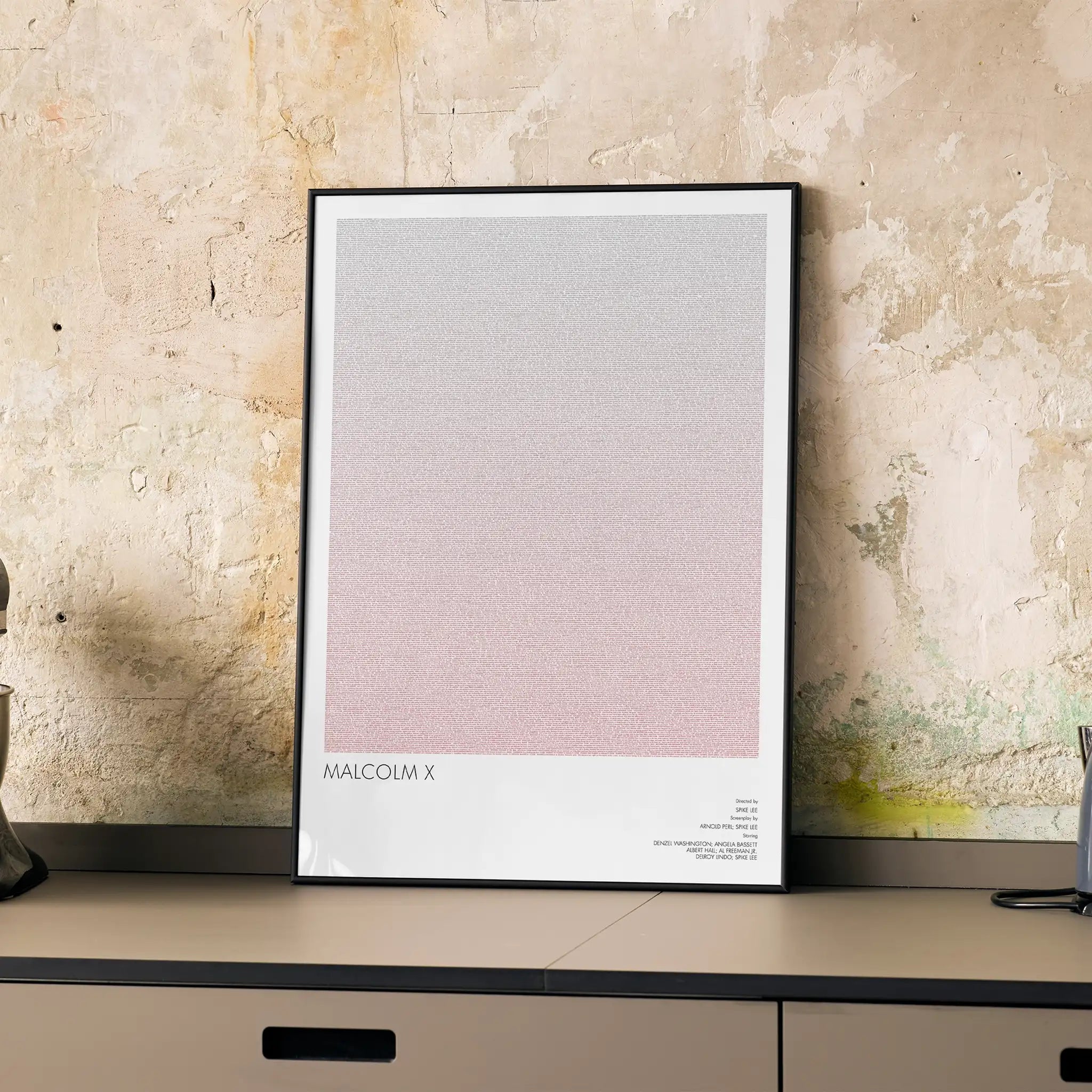 A framed Malcolm X movie script poster displayed on a cabinet in a minimalist interior.