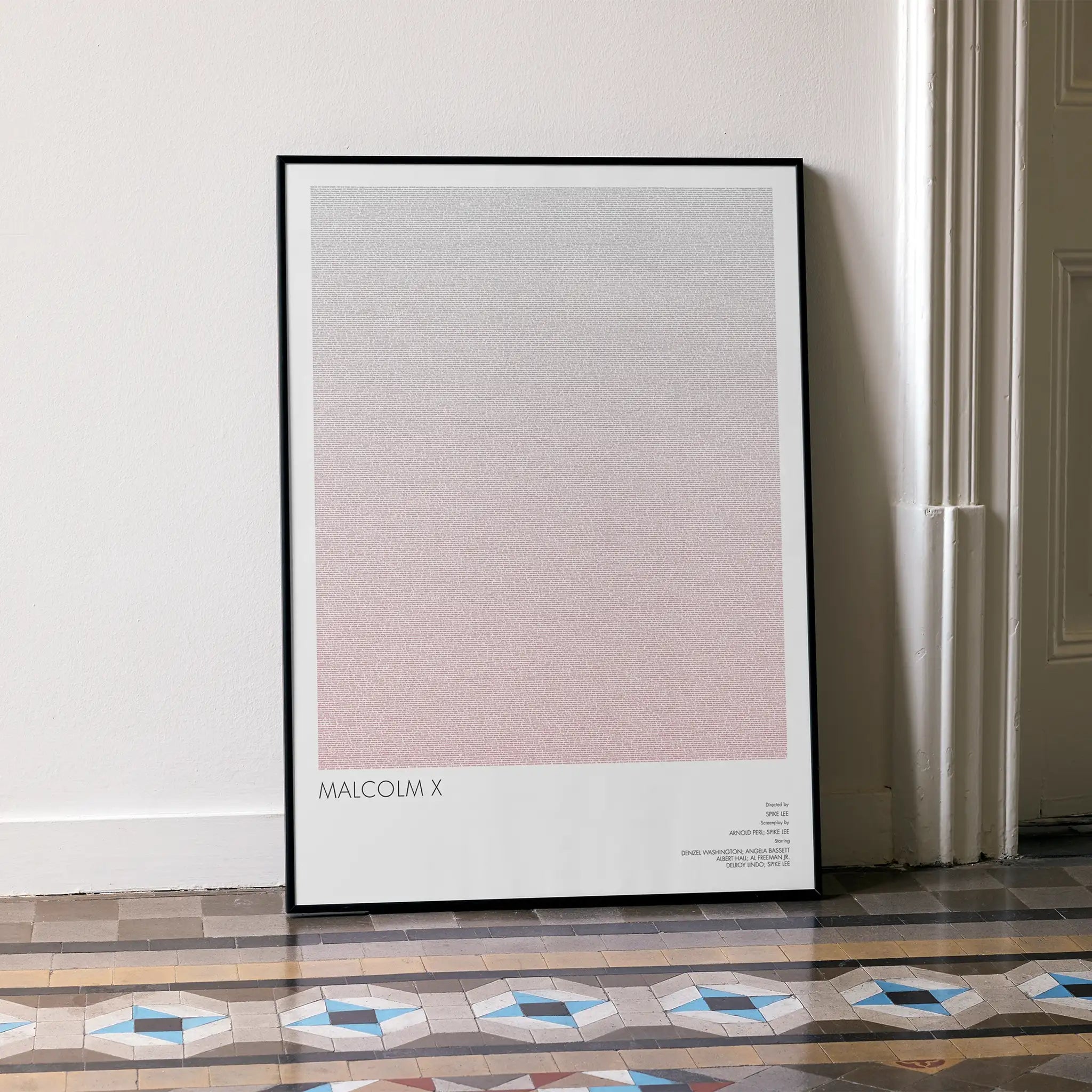 A framed Malcolm X movie script poster leaning against a wall in a minimalist interior.