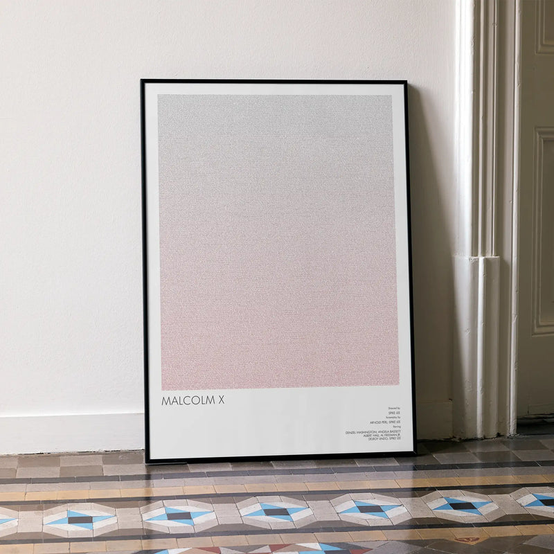 A framed Malcolm X movie script poster leaning against a wall in a minimalist interior.