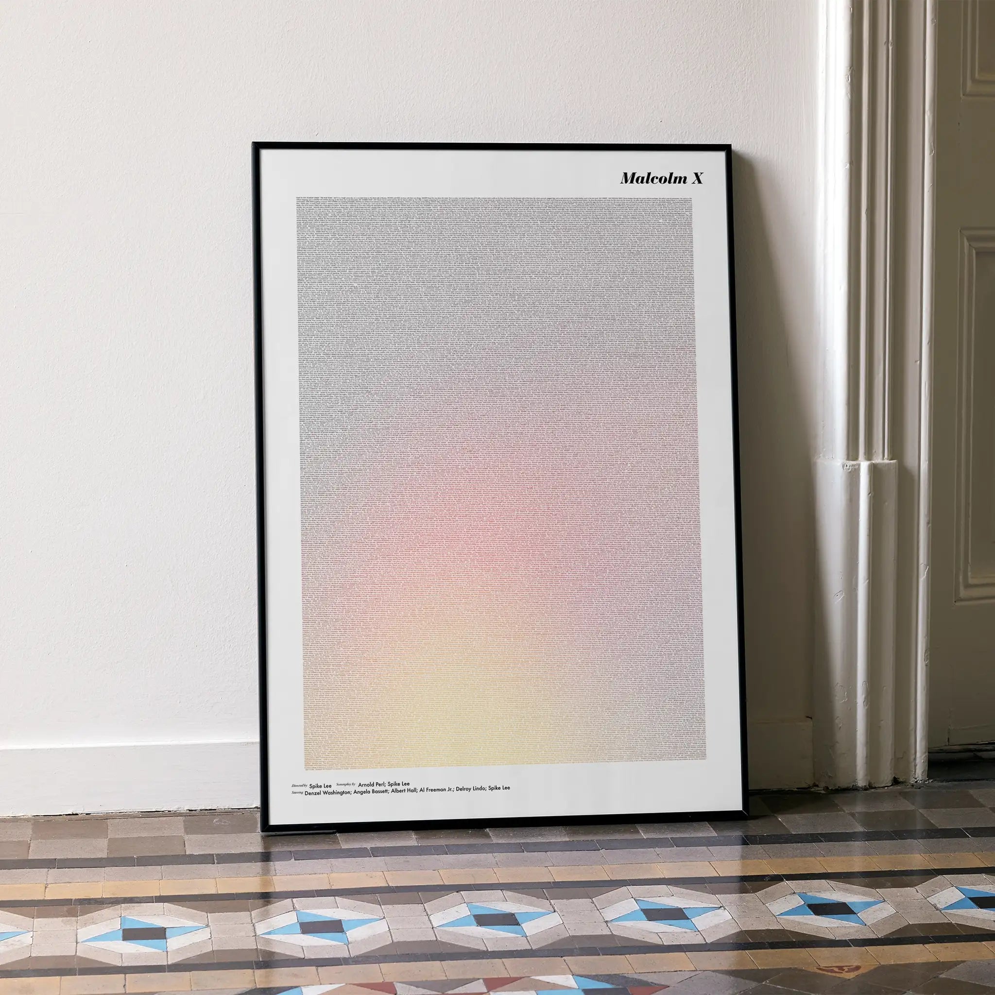 A framed Malcolm X movie script poster leaning against a wall in a minimalist interior.