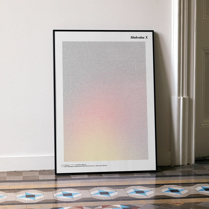 A framed Malcolm X movie script poster leaning against a wall in a minimalist interior.