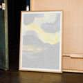 Framed abstract Malcolm X art piece with yellow and gray colors leaning against a wooden cabinet.