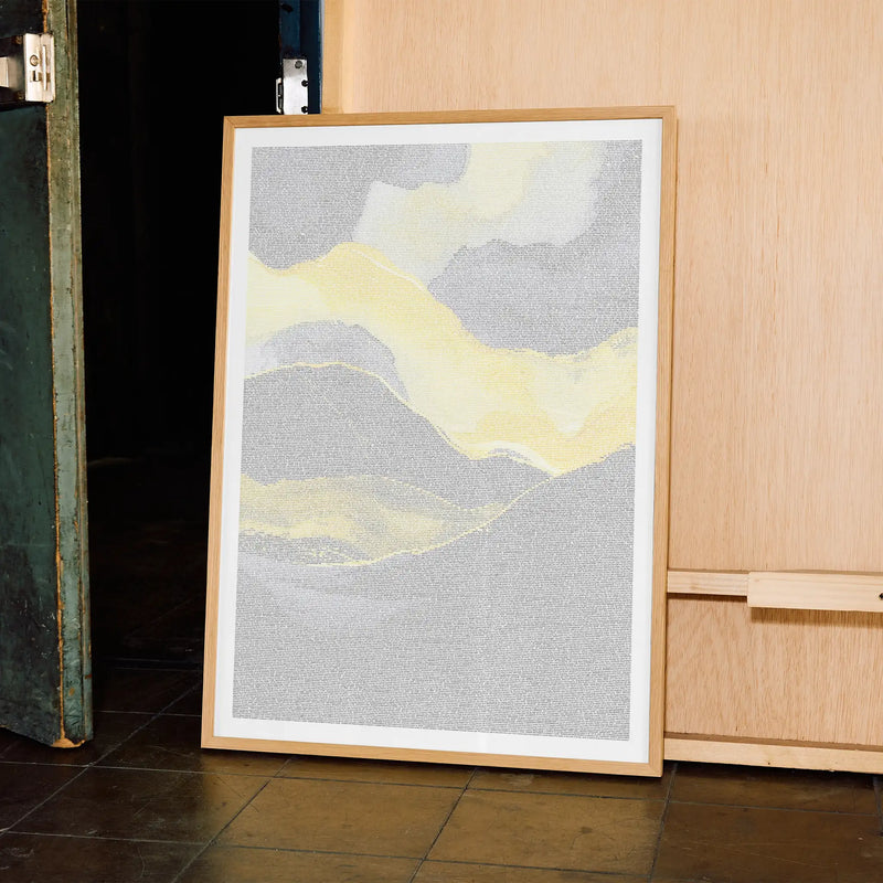 Framed abstract Malcolm X art piece with yellow and gray colors leaning against a wooden cabinet.