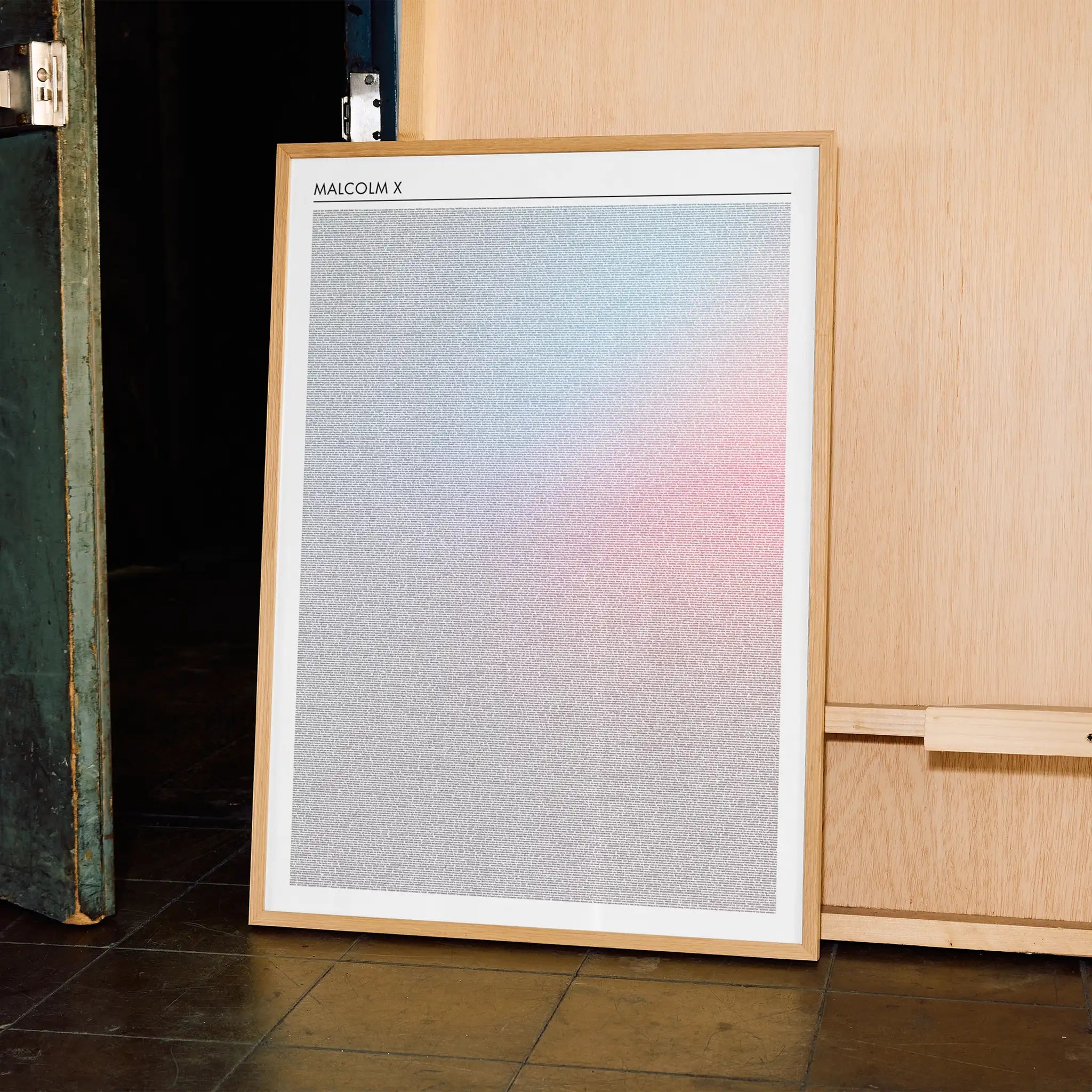 Framed Malcolm X artwork with a gradient leaning against a wooden cabinet.