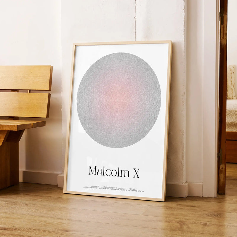 Framed Malcolm X movie poster artwork with a circular aura design and text on a wooden floor.