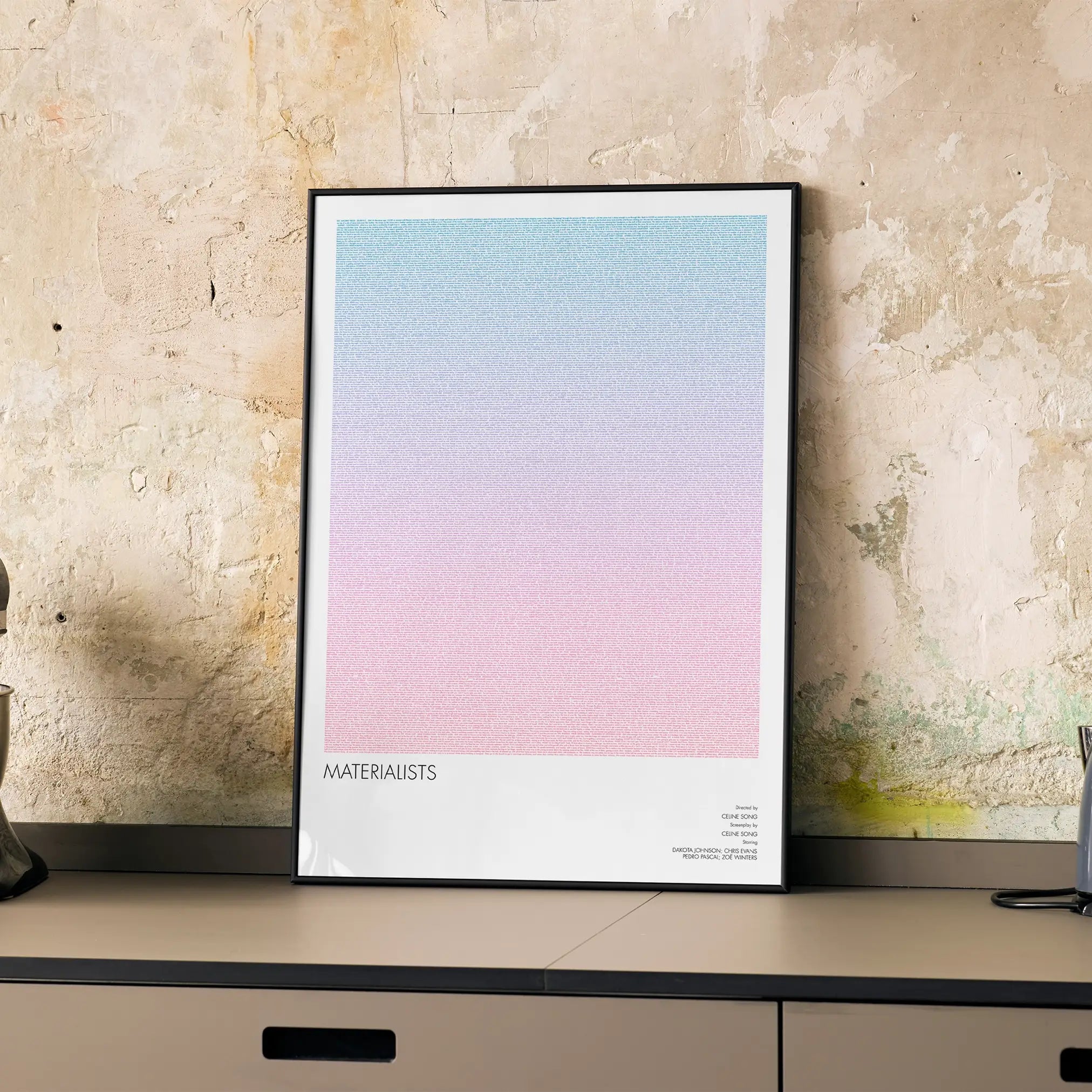A framed Materialists movie script poster displayed on a cabinet in a minimalist interior.