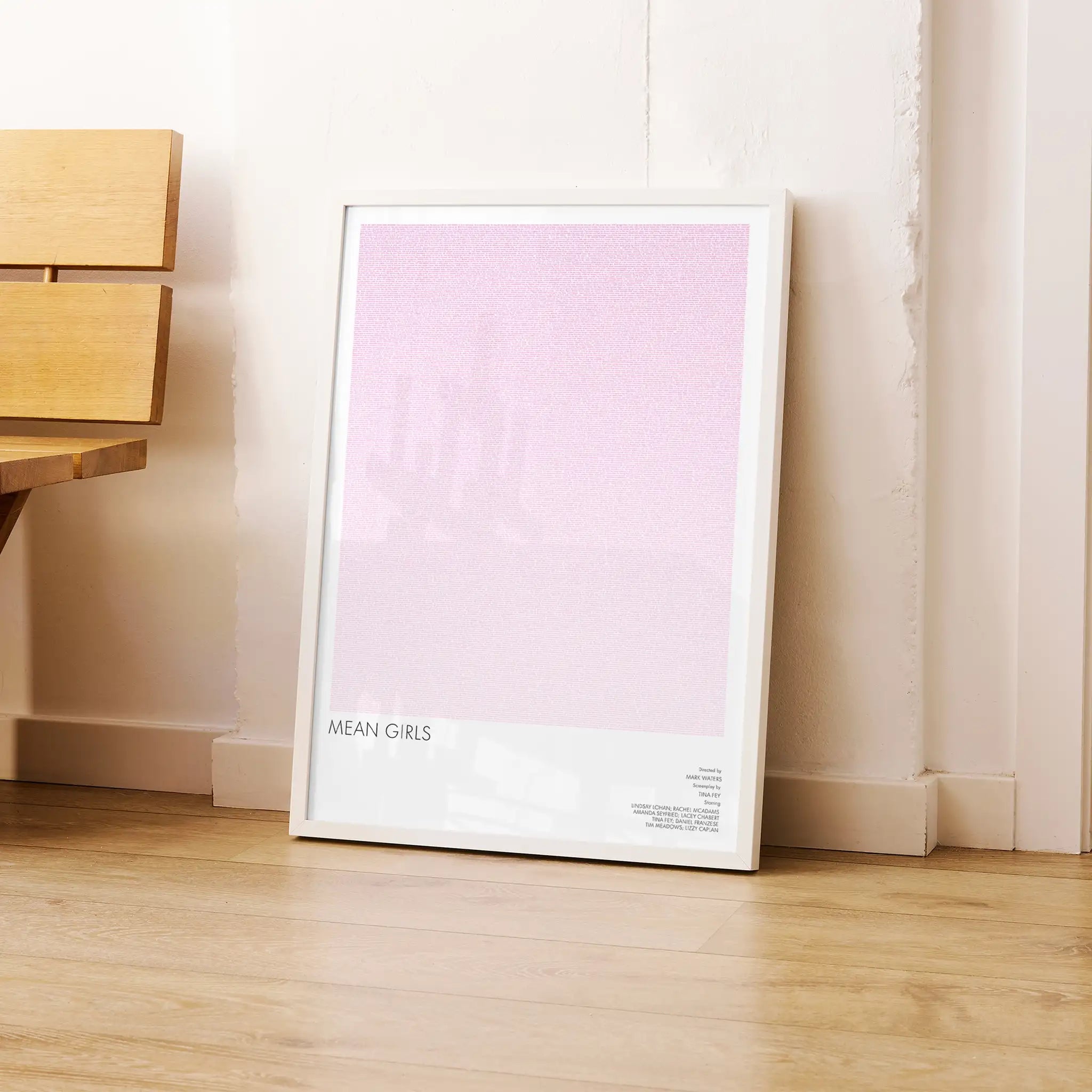 Framed poster titled 'Mean Girls' on a wooden floor against a white wall.
