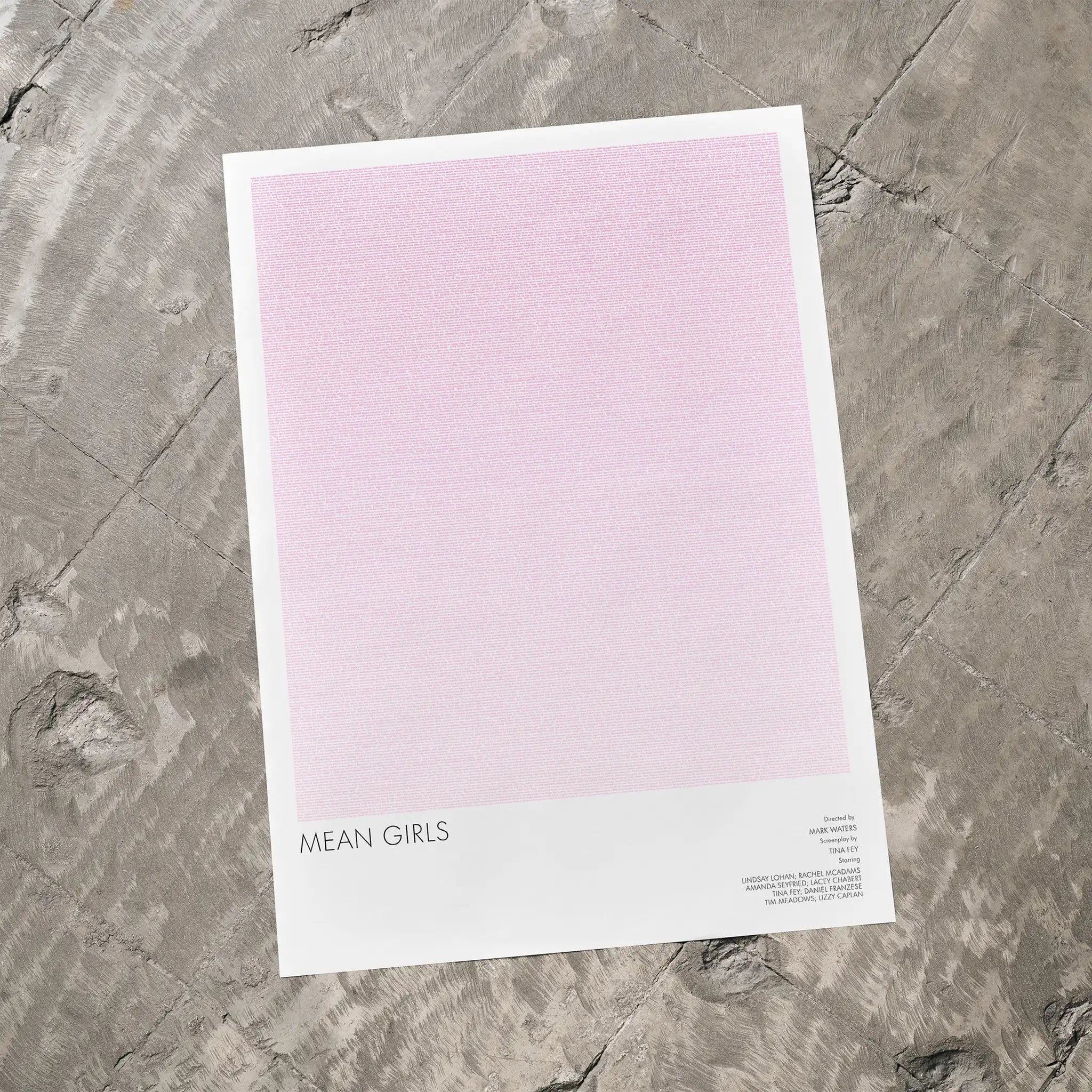Mean Girls movie poster on a pink background, lying on a textured gray surface.