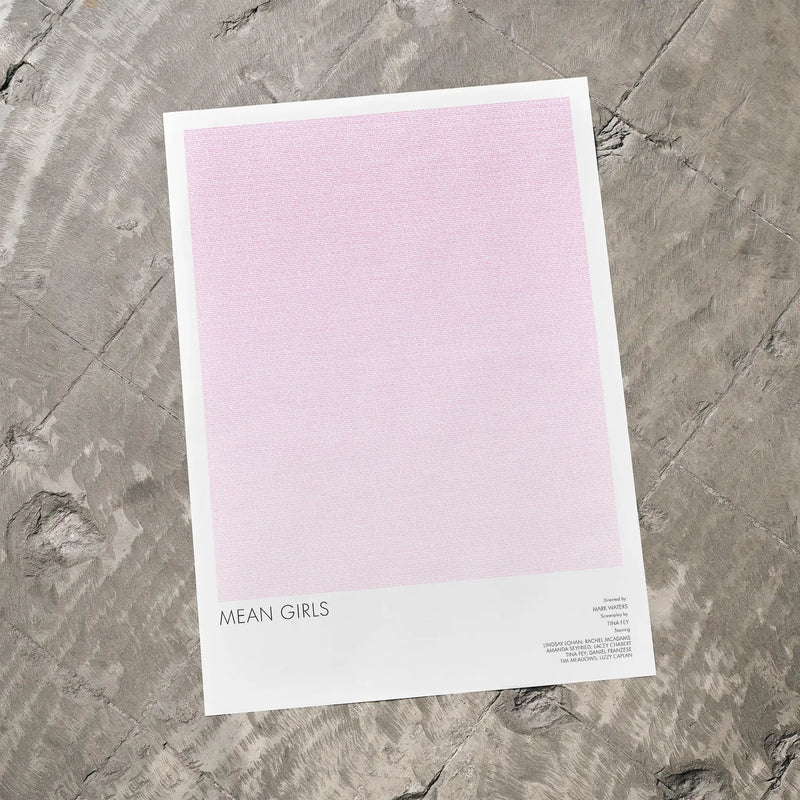 Mean Girls movie poster on a pink background, lying on a textured gray surface.