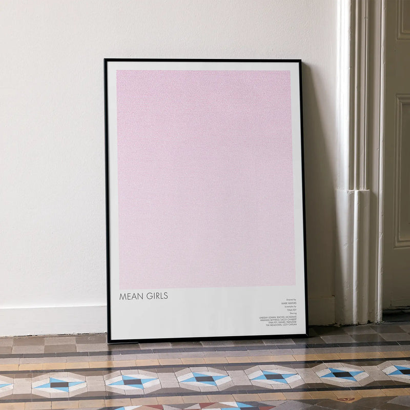 Framed poster with 'Mean Girls' text on a light pink background in a room with patterned floor.