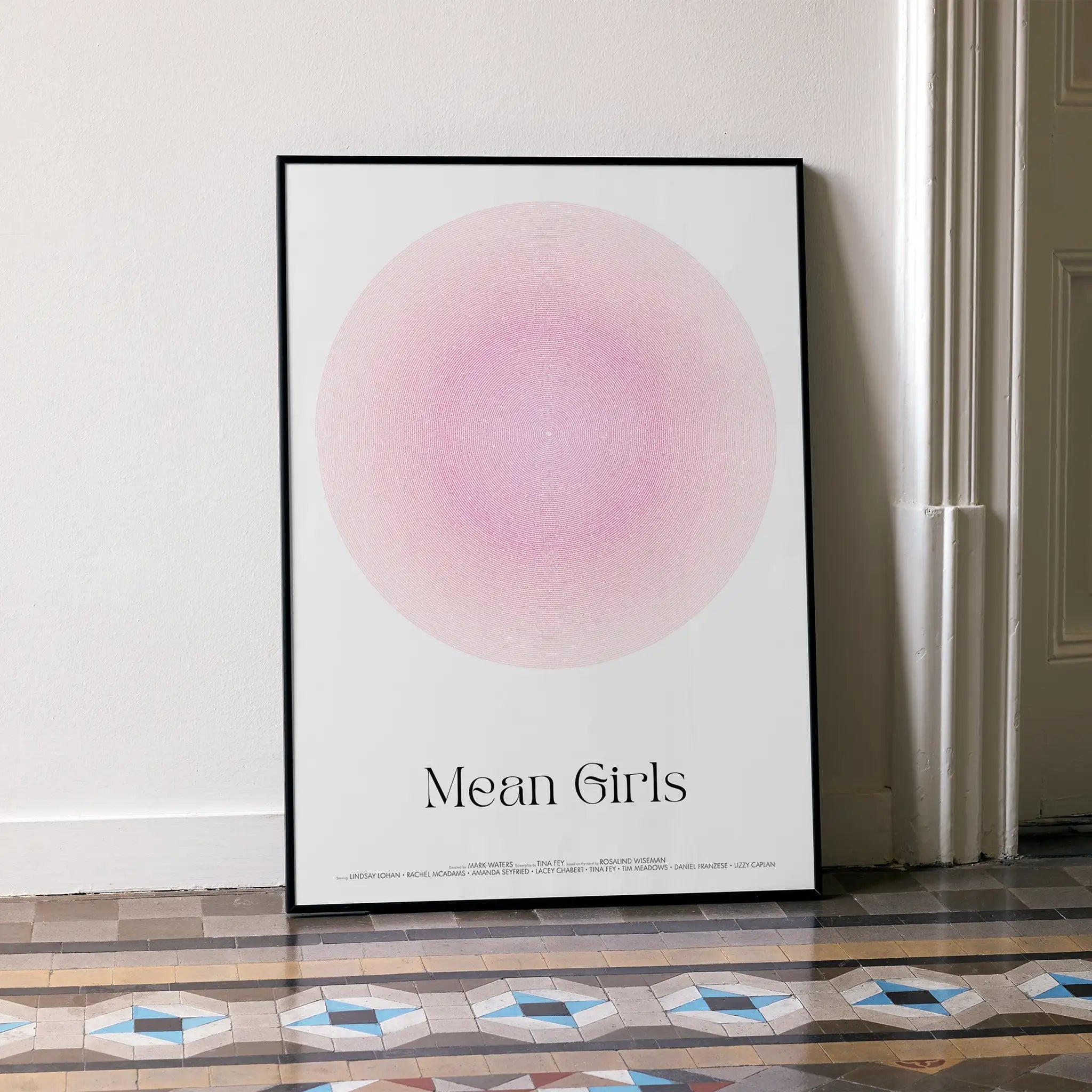 Framed Mean Girls script movie poster leaning on white wall.