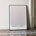 A framed Mistress America movie script poster leaning against a wall in a minimalist interior.