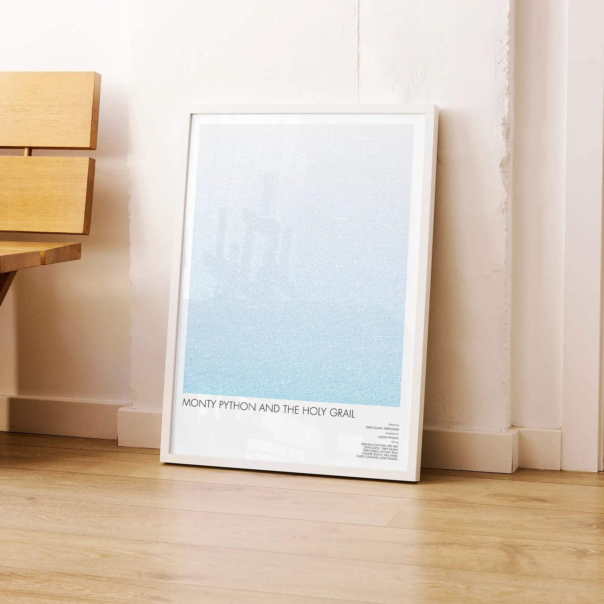 A framed Monty Python and the Holy Grail movie script poster leaning against a wall in a modern interior.