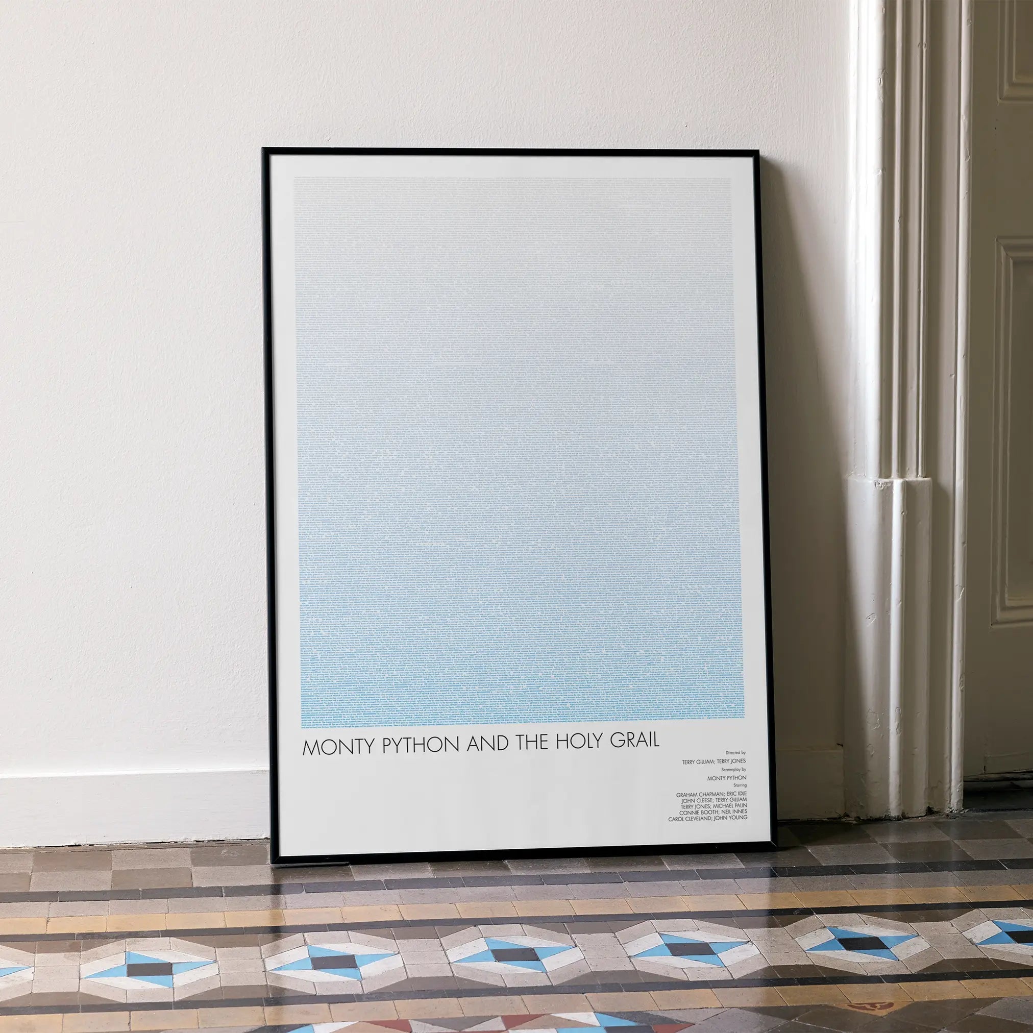 A framed Monty Python and the Holy Grail movie script poster leaning against a wall in a minimalist interior.