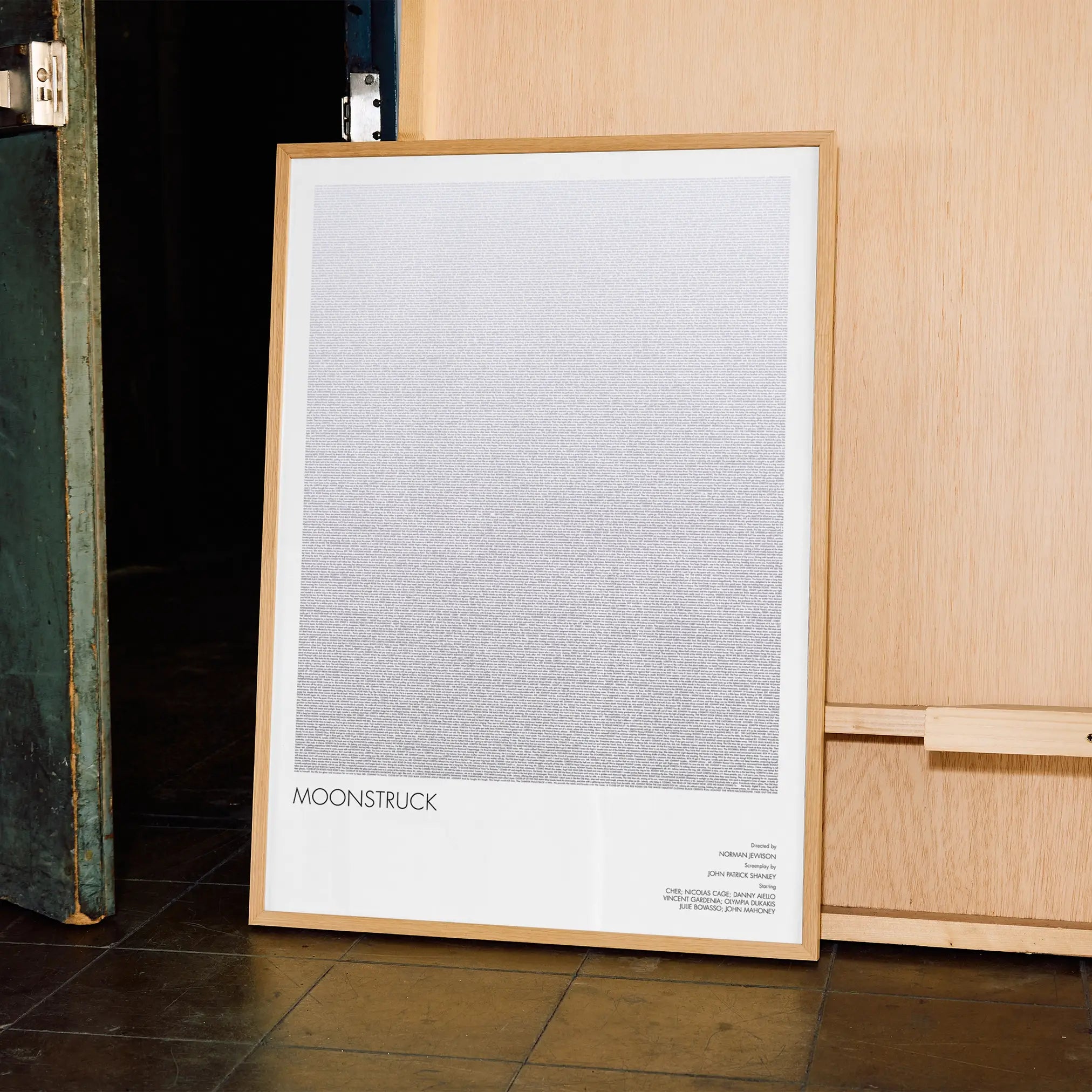 Framed Moonstruck poster with a gradient design leaning against a wooden cabinet.