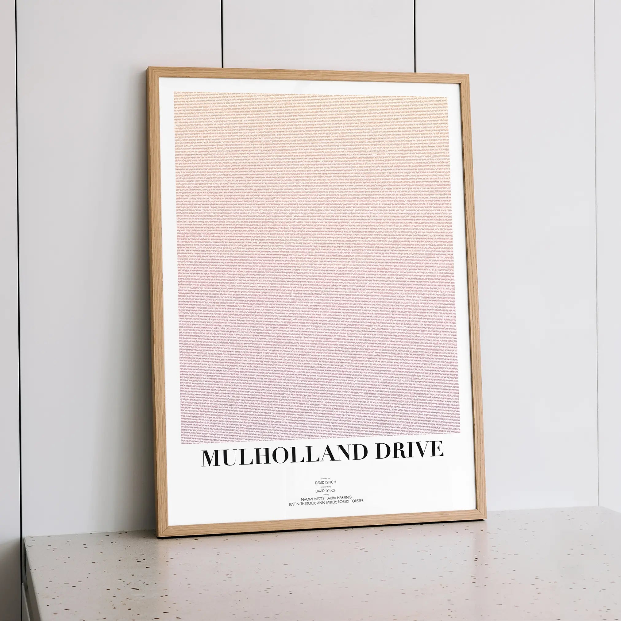Framed poster with 'Mulholland Drive' text on a light background, leaning against a white wall.