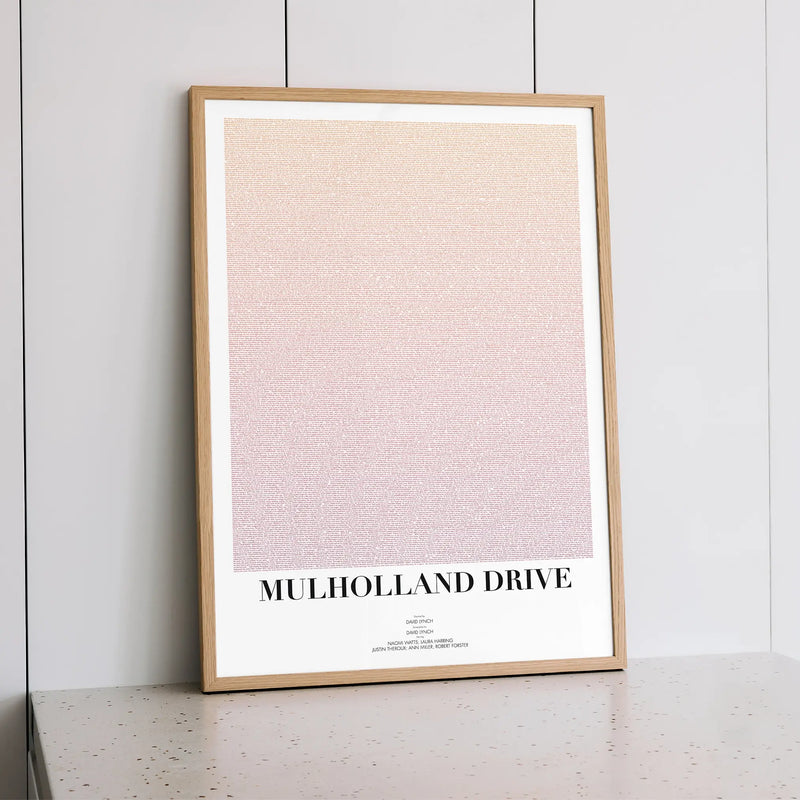 Framed poster with 'Mulholland Drive' text on a light background, leaning against a white wall.