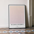 Framed poster with 'Mulholland Drive' text on a neutral background, leaning against a wall.
