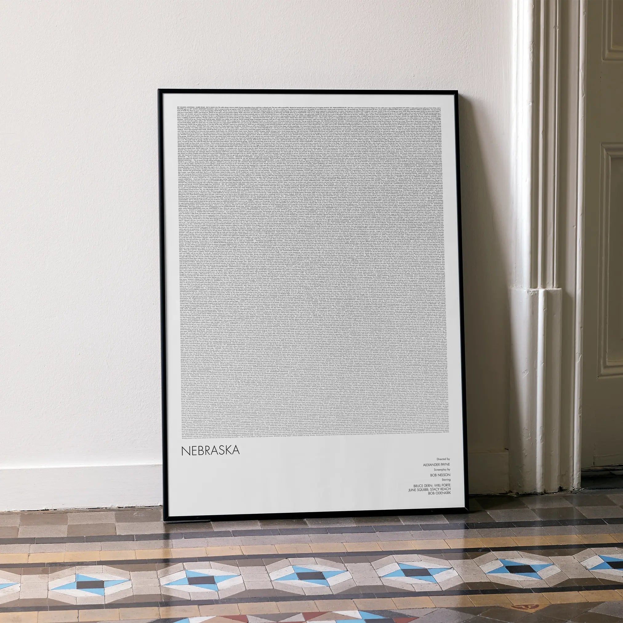 A framed Nebraska movie script poster leaning against a wall in a minimalist interior.