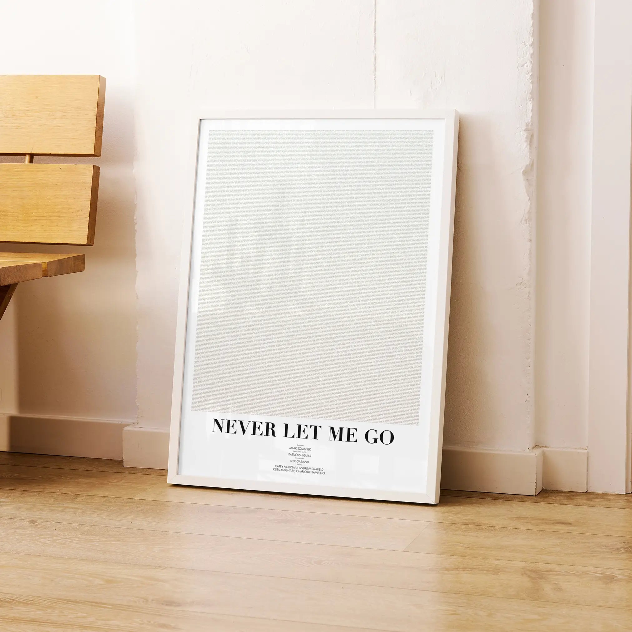 A framed Never Let Me Go movie script poster leaning against a wall in a modern interior.