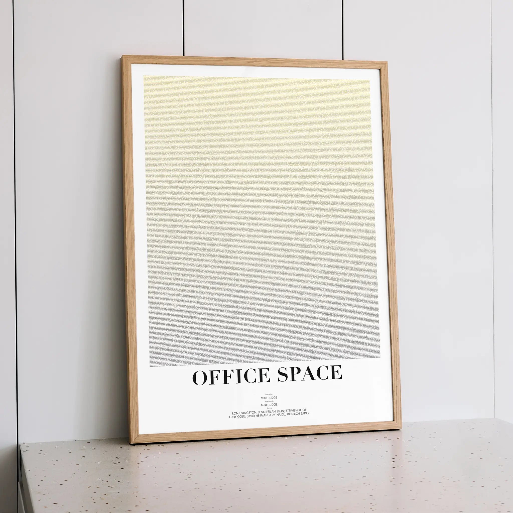 Framed poster with 'OFFICE SPACE' text on a light background, leaning against a grey wall.