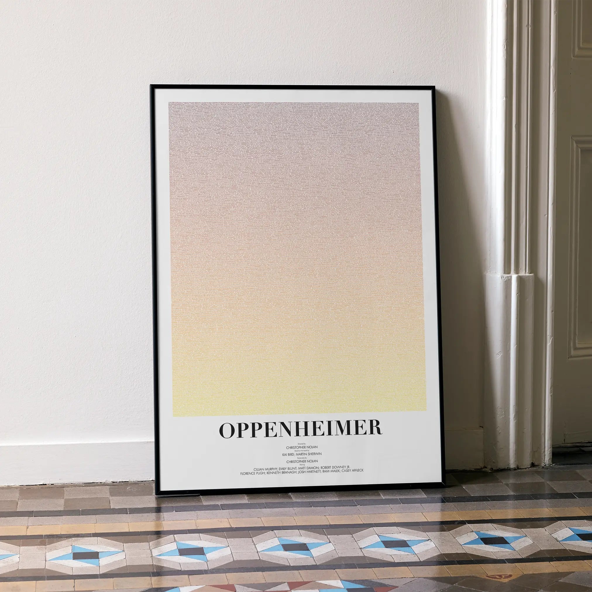A framed Oppenheimer movie script poster leaning against a wall in a minimalist interior.