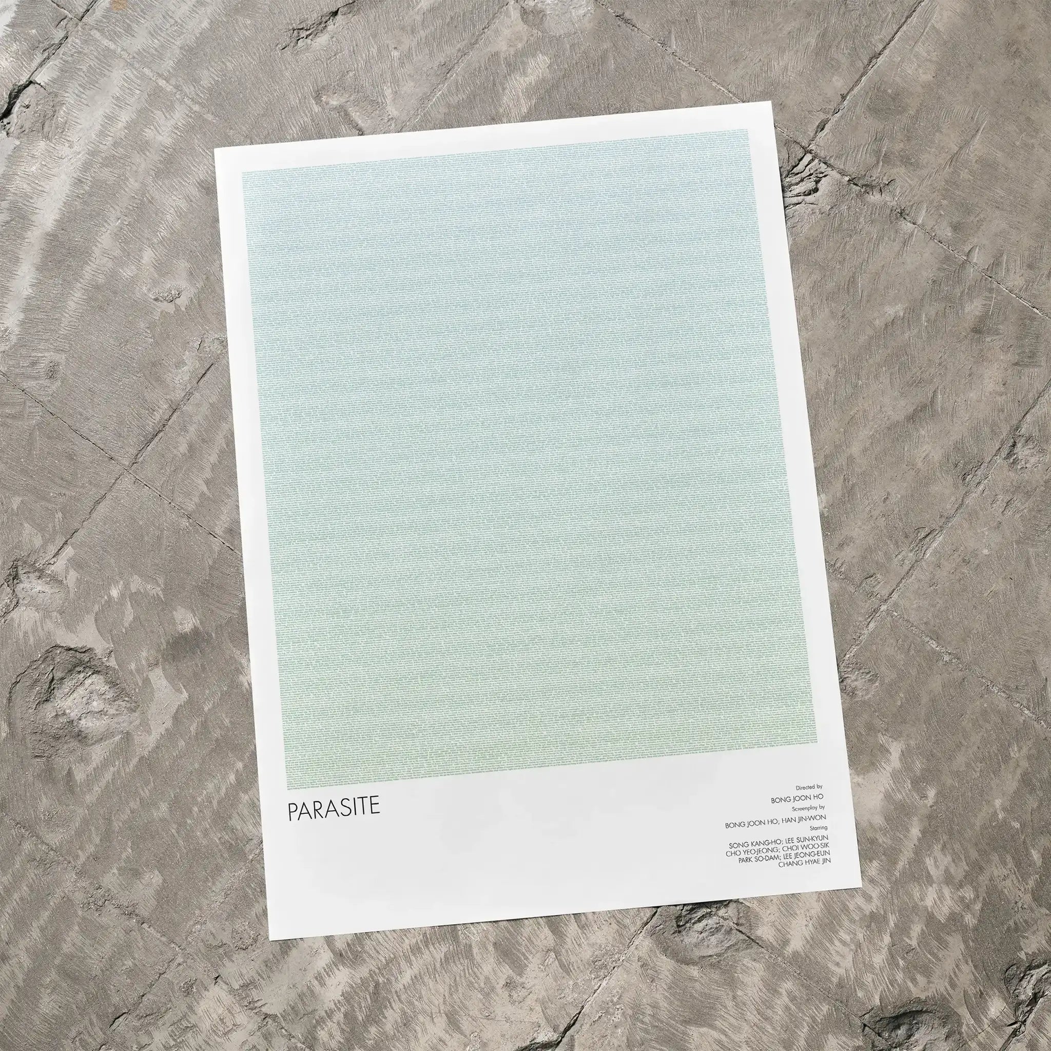 A Parasite movie script poster laid flat on a textured floor surface.