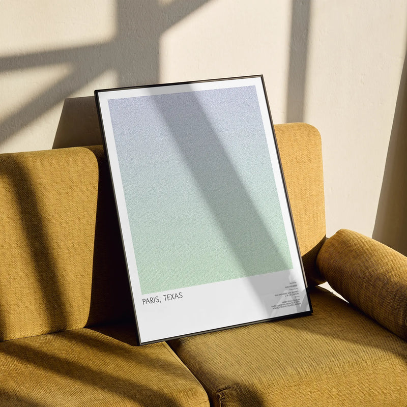 A framed Paris, Texas movie poster lays on a yellow vintage sofa.