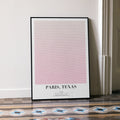 A framed Paris, Texas movie script poster leaning against a wall in a minimalist interior.
