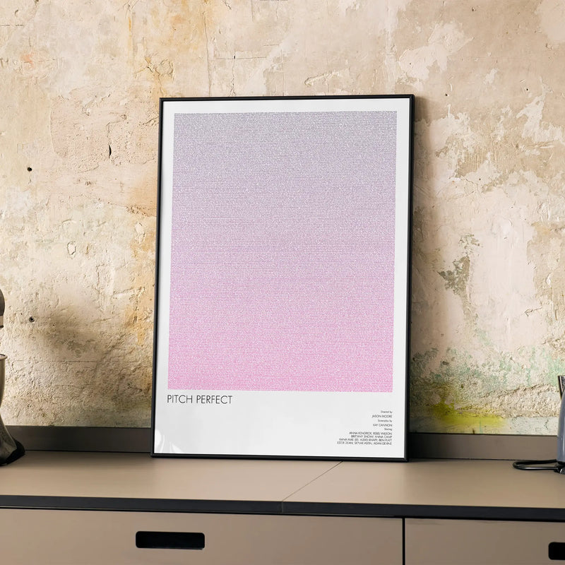 A framed Pitch Perfect movie script poster displayed on a cabinet in a minimalist interior.