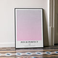 A framed Pitch Perfect movie script poster leaning against a wall in a minimalist interior.