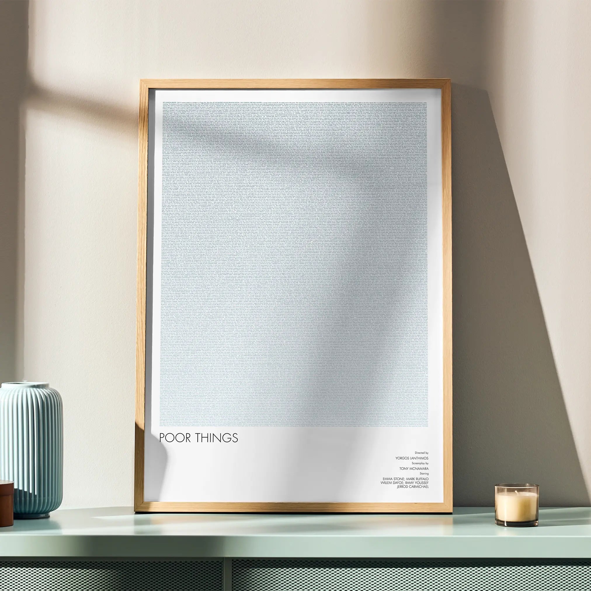 A framed Poor Things movie script poster displayed in a simple modern interior.