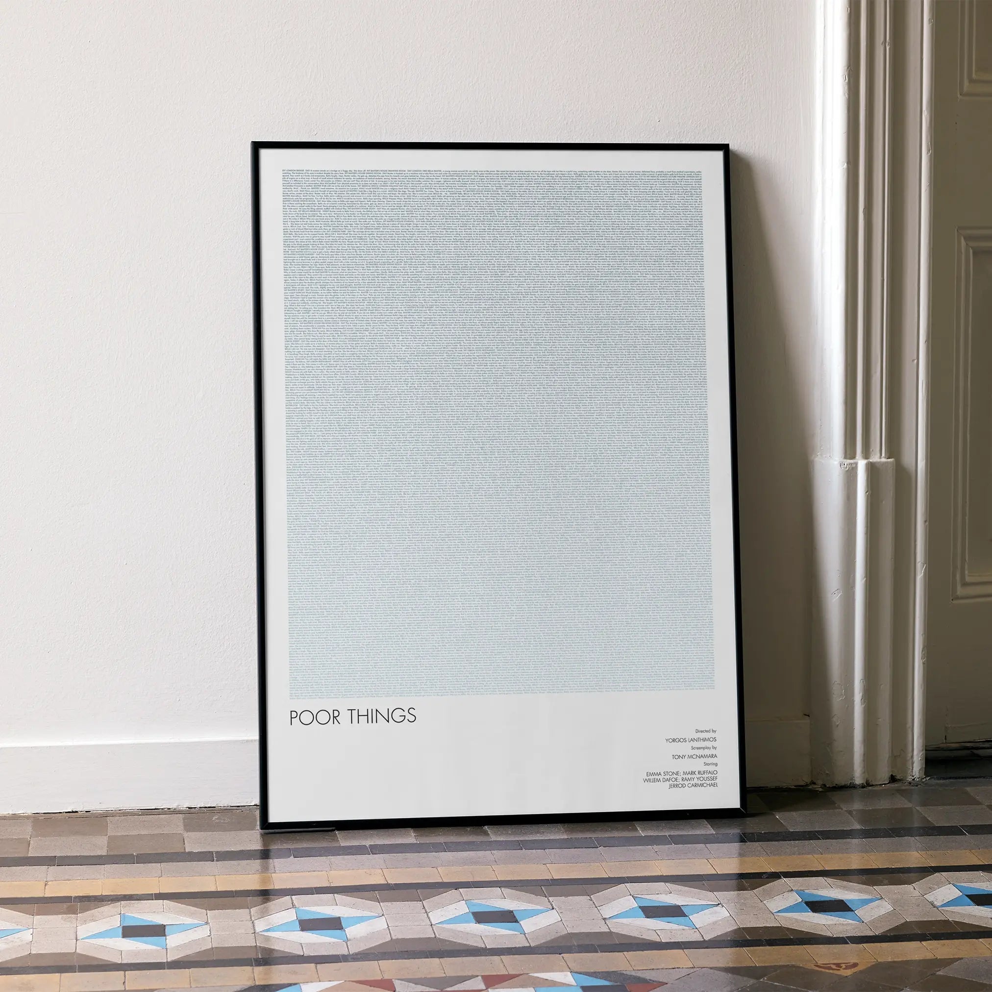 A framed Poor Things movie script poster leaning against a wall in a minimalist interior.
