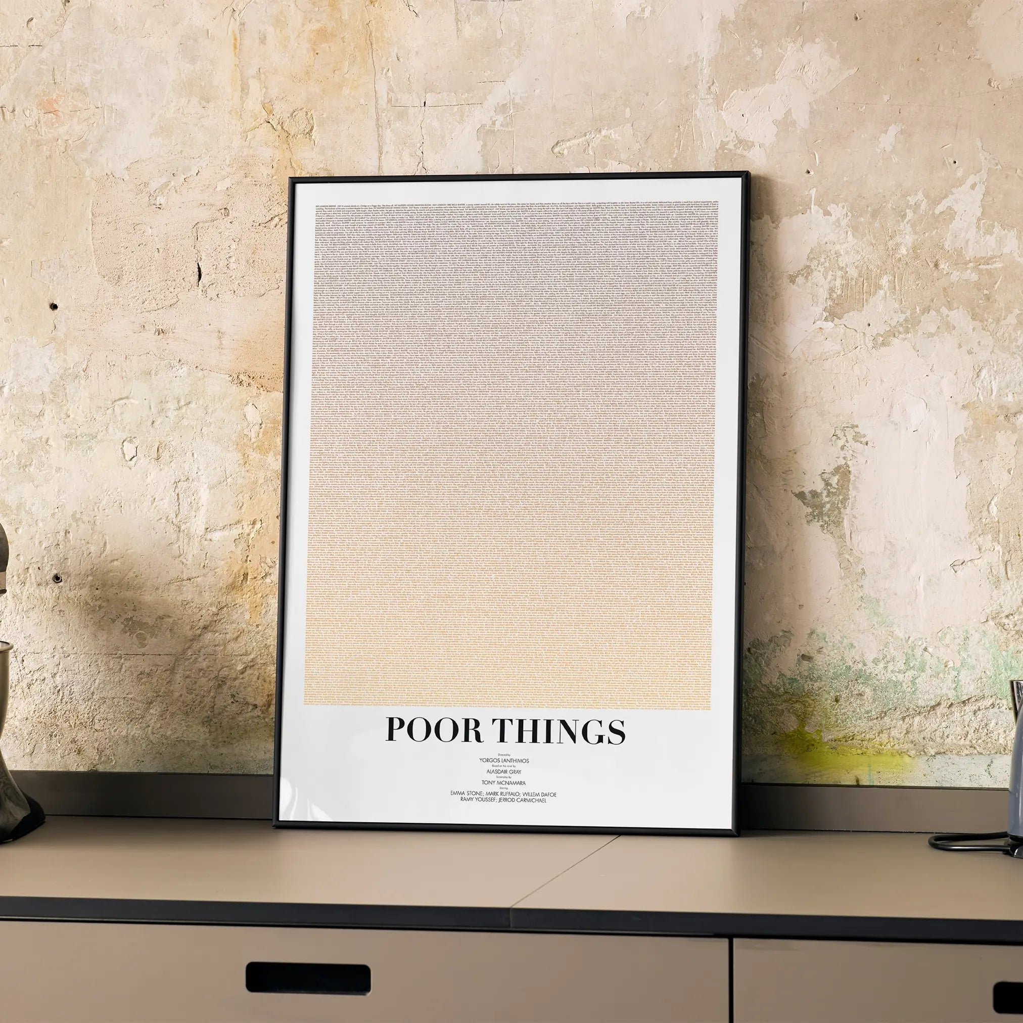 A framed Poor Things movie script poster displayed on a cabinet in a minimalist interior.