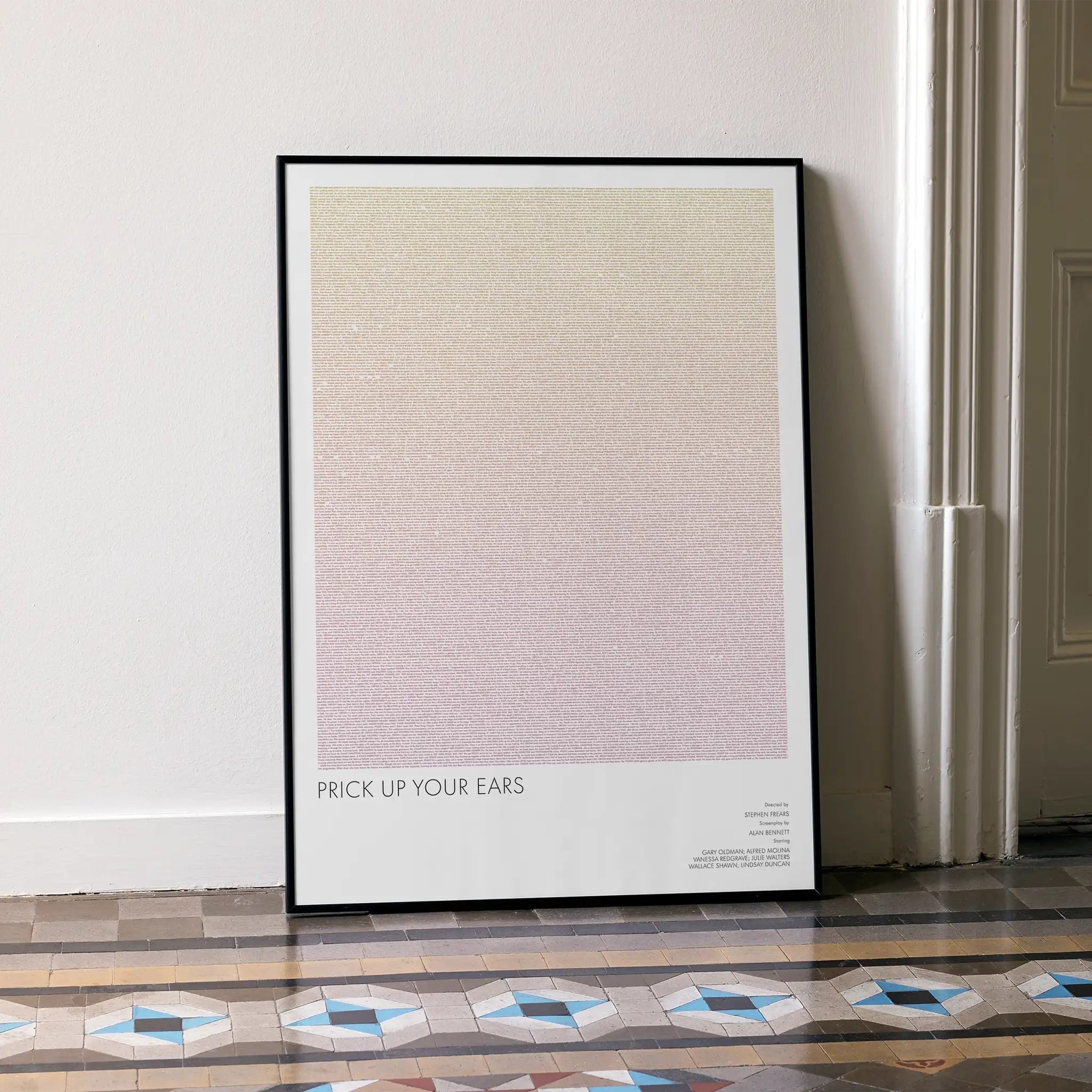 A framed Prick Up Your Ears movie script poster leaning against a wall in a minimalist interior.