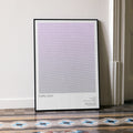 A framed Purple Rain movie script poster leaning against a wall in a minimalist interior.
