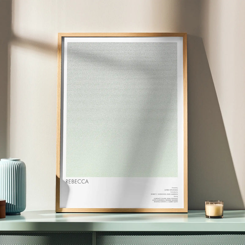 A framed movie poster for Hitchcock's "Rebecca", sits on a green sideboard.