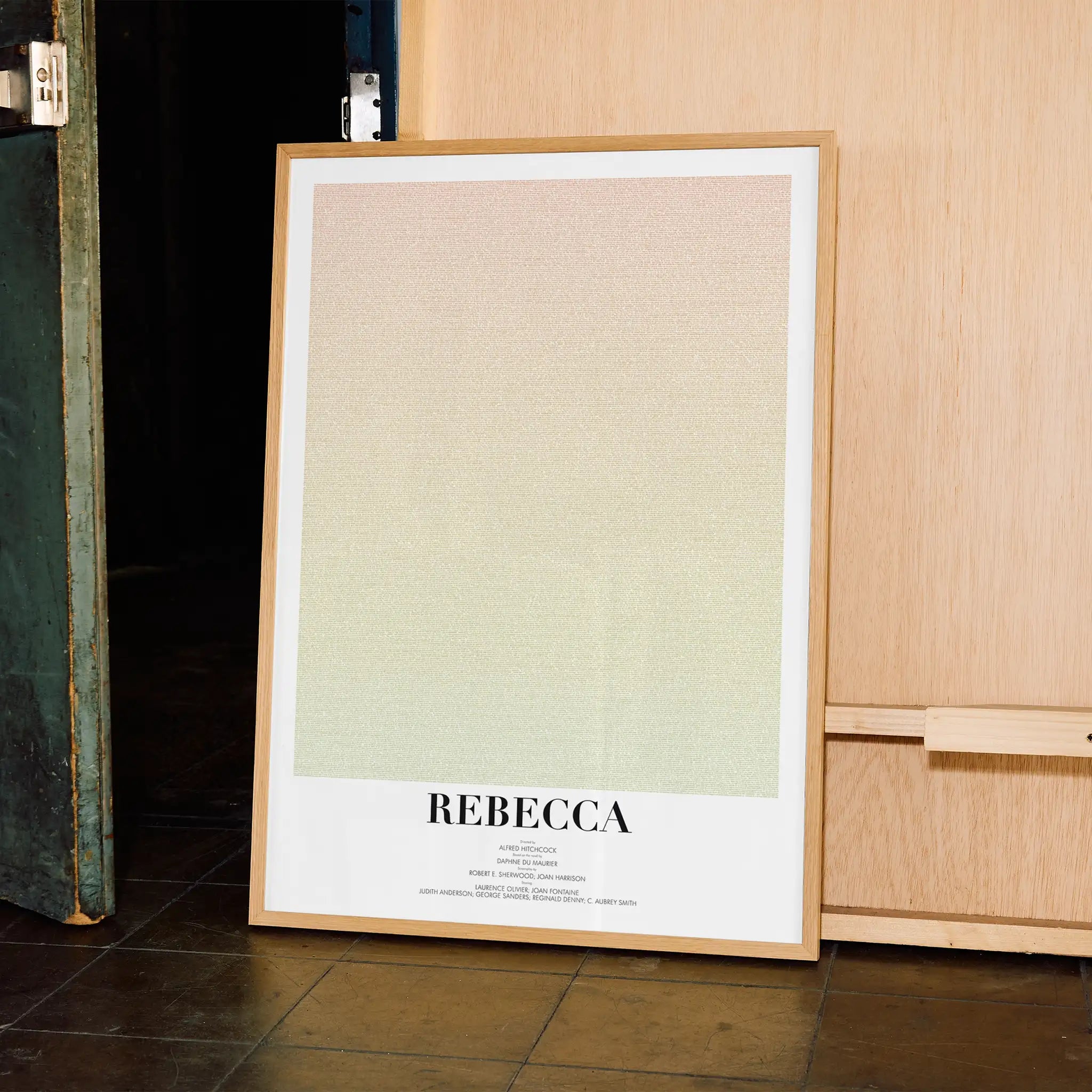 A framed poster for Hitchcock's "Rebecca" leaning against a wooden wall.